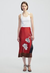 Rode satijnen rok met bloemenprint en een bruine zoom, gedragen met een witte tanktop. Heeft een aansluitende snit en een gladde textuur.
