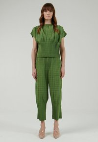 Conjunto texturizado de dos piezas en verde, con top plisado y pantalones ajustados a juego. Presenta una tela suave y un ajuste relajado, combinado con tacones transparentes.