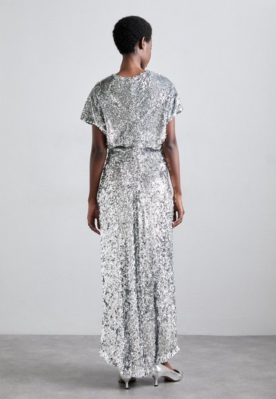 Silver sequin dress with short sleeves, flowing silhouette, and a scoop back. Smooth texture and high slit, paired with silver shoes.