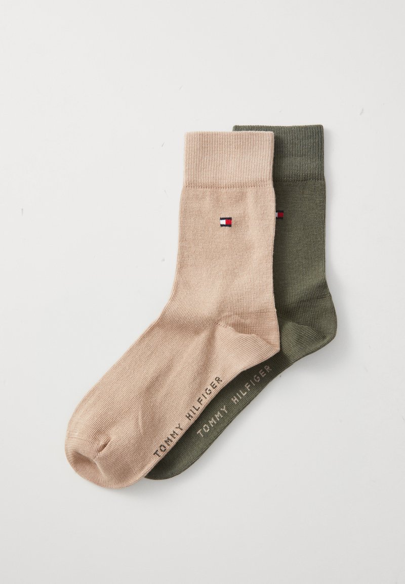 Dos pares de calcetines de tripulación, uno beige y otro verde oliva, ambos con pequeño logotipo de Tommy Hilfiger y nombre de la marca en el arco del pie.