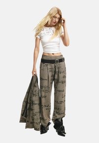 Valge lühikeste varrukatega pluus musta tekstiga, millele on lisatud kõrge vöökohaga ruudulised püksid käekirjaga mustritega ning mustad kontsakingad.