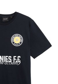 Marinblå bomullströja med en rund logotyp som har en gul blomma och texten "SHINING OVER SCOTLAND" på bröstet, samt stor vit text "SUNNIES F.C." nedanför.