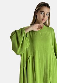 Lös sittande klänning med långa ärmar i livlig limegrön, med texturerad tyg, ballongärmar och sidofickor.
