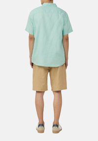 Lichtgroene korte mouwen shirt van linnen, gecombineerd met tan korte broek. Het shirt heeft een button-down kraag en een relaxte pasvorm.