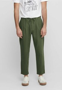 Groene linnen broeken met een relaxte pasvorm, een trekkoord in de taille en een taps toelopende pijp. Gecombineerd met een witte graphic t-shirt en witte sneakers.