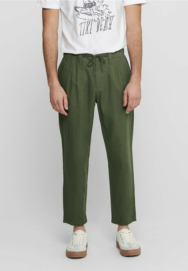 Groene linnen broeken met een relaxte pasvorm, een trekkoord in de taille en een taps toelopende pijp. Gecombineerd met een witte graphic t-shirt en witte sneakers.