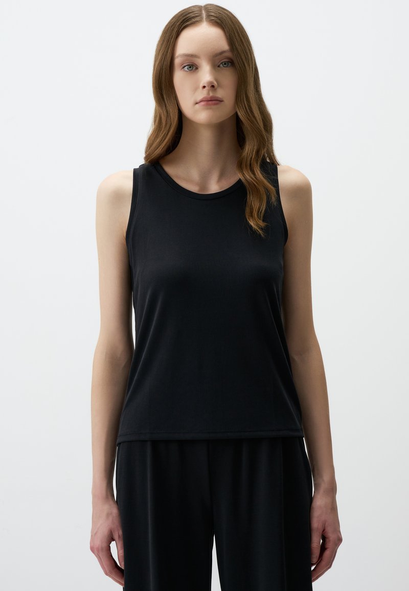 Top nero senza maniche realizzato in un tessuto liscio, caratterizzato da un girocollo e una vestibilità comoda, indossato con pantaloni neri coordinati.