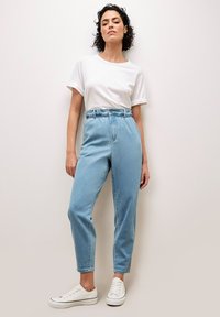 Jeans azzurri a vita alta con vita svasata e vestibilità rilassata, abbinati a una t-shirt bianca a maniche corte e sneakers bianche.