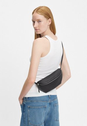 Schwarze Leder-Bauchtasche mit glatter Textur und geschwungener Form, ausgestattet mit einem oberen Reißverschluss und einem verstellbaren Gurt, der über den Körper getragen wird.