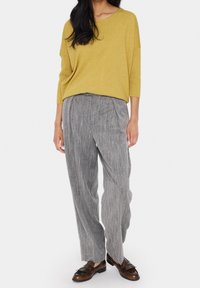 Pull en tricot jaune moutarde à manches trois-quarts associé à un pantalon plissé rayé gris et des mocassins marron.