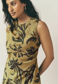 Rochie fără mâneci din material verde măsliniu, cu un model floral negru. Textură netedă, cu un design ușor drapat și decolteu rotund.