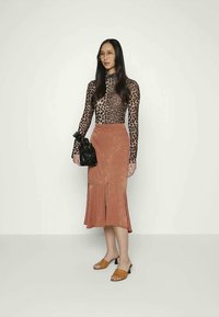 Top de mangas longas com padrão de leopardo, saia midi na cor ferrugem com bainha assimétrica, sandálias slide em tom baunilha e uma bolsa de mão preta. Texturas suaves em geral.