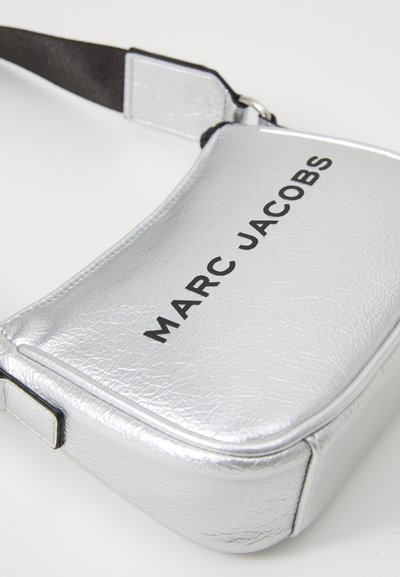 Sølv crossover-veske med teksturert finish, med en svart "MARCB JACOBS" logo på forsiden, og en svart stroppfeste.