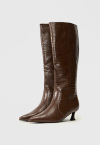 Bottes knee-high en faux cuir crocodile brun avec des bouts pointus, des talons bas et une texture lisse. Présentent une finition brillante et un motif en relief.