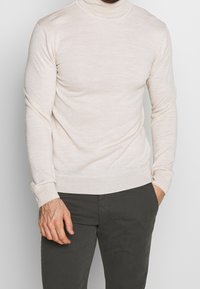 Helle beige Rollkragensweater aus feinem Strickstoff. Verfügt über lange Ärmel und ein tailliertes Design mit strukturierter Optik.