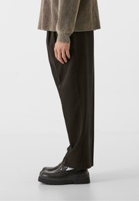 Pantalones negros de pierna ancha combinados con zapatos negros gruesos. La parte superior es un suéter de textura ligera con puños acanalados. Vista lateral.
