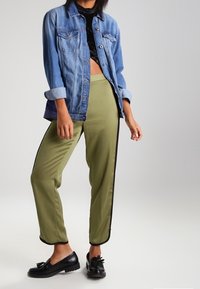 Džínová bunda v světle modré barvě, krátký střih se zapínáním na knoflíky, doplněná olivově zelenými kalhotami s černými bočními pruhy. Černé boty.