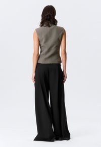 Haut sans manches couleur vert olive avec un tissu texturé, coupe ajustée et ourlet légèrement asymétrique. Associé à un pantalon noir taille haute, jambes larges.