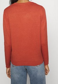 Maglione rosso lavorato a maglia con colletto rotondo e maniche lunghe, con orlo a coste. Abbinato a jeans in denim blu chiaro.