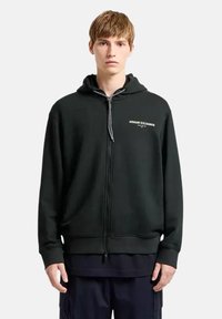 Felpa nera con zip, tasche anteriori, cappuccio regolabile con cordino e dettaglio del logo. Tessuto morbido, polsini e orlo a costine.
