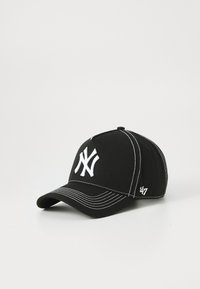 Svart baseballcaps med en fremtredende hvit New York Yankees-logo og hvite sømdetaljer, vist på en lys bakgrunn.