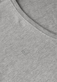 Graues Baumwoll-T-Shirt mit Rundhalsausschnitt und einer dezenten strukturierten Oberfläche. Besitzt ein kleines, geprägtes Logo in der unteren linken Ecke.