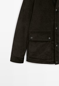 Giacca in corduroy marrone scuro con superficie strutturata, chiusura con bottoni, due tasche a patta e dettagli cuciti ai polsini e all'orlo.