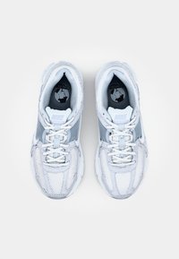 Sapatilhas Nike com um superior de malha predominantemente branca com detalhes cinzentos, sola branca espessa e marcação azul na língua.