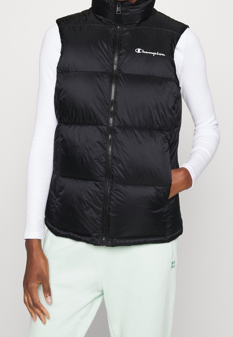 Svart pufferväst med hög krage, framdragkedja och logotyp. Tillverkad av glänsande material, med ett kviltat mönster och sidofickor.