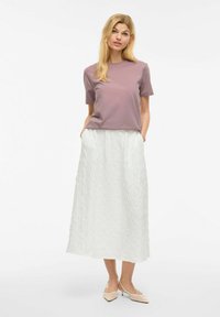 Lavendelkleurig t-shirt met korte mouwen gecombineerd met een textuur witte maxi rok, met zijzakken. Model draagt blootkleurige puntige hakken.