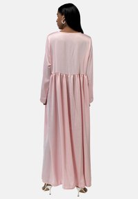Vestido maxi rosa de manga larga, hecho de un tejido suave y liso, con una cintura fruncida y una falda fluida. Cuello redondo sencillo, sin patrones visibles.