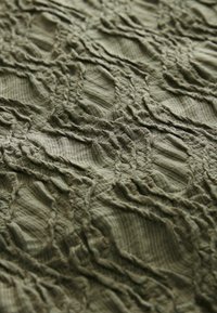 Texturerad olivgrön tyg med ett krusigt mönster som har vågiga detaljer och varierande horisontella och vertikala linjer. Mjuk och lätt material.