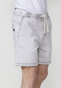 Pantalones cortos de mezclilla gris claro con cinturilla elástica, cierre con cordón, bolsillos laterales y dobladillo cosido. Textura sutil en toda la prenda.