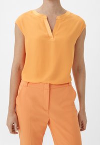 Orange, kortærmet bluse med V-hals og satin kant. Glat stof, parret med matchende orange bukser, hvilket skaber et koordineret look.