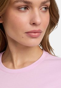 Helles rosa Kurzarmhemd mit rundem Ausschnitt, aus glattem Stoff und mit klaren Nähten entlang des Kragens.