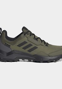 Zelená turistická obuv s černými detaily, strukturovaným povrchem, robustní podrážkou a třemi tmavými pruhy na boku, navržená pro venkovní výkon.