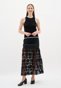 Black sleeveless top with white trim, paired with a black lace skirt featuring floral patterns, and holding a small black handbag. Black heels.