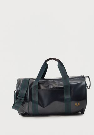 Czarna cylindryczna torba sportowa z zielonymi podwójnymi uchwytami, odpinanym paskiem na ramię, przednią kieszenią i małym złotym emblematem z boku.