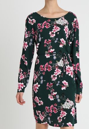 Robe fleurie à manches longues, base vert foncé, motif floral rose et blanc, et une ceinture à nouer à la taille. Tissu doux, design ajusté.