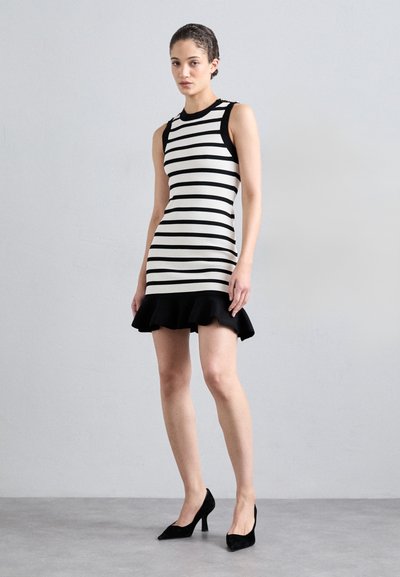 Black and white striped sleeveless dress with a fitted bodice and flared black ruffled hem. Model wears black pointed-toe heels.