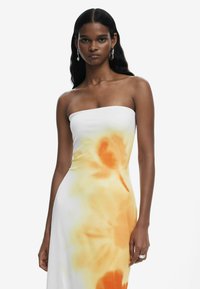 Strapless dress made of soft fabric, featuring a gradient of white to soft orange floral patterns. Smooth texture with a fitted silhouette.