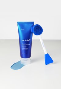 Blaues Röhrchen der Medicube Zero Pore Blackhead Mud Maske mit weißem Deckel, daneben ein blauer Silikonapplikator. Helle blaue Maske ist auf einer weißen Oberfläche verschüttet.