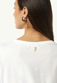 Weißes Baumwoll-T-Shirt mit Rundhalsausschnitt und kurzen Ärmeln, mit kleinem goldenen Logo am oberen Rücken. Glatte Textur.