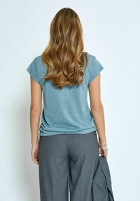 Gaiši zils īsām piedurknēm tops ar mīkstu, mirdzošu tekstūru; apvienots ar pelēkām platām biksēm. Topam ir brīvs griezums un noapaļota apakša.