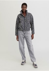Fleece zip-up jack in donkerblauw met lichtblauw abstract patroon; voorzien van een hoge kraag en een relaxte pasvorm. Gecombineerd met lichtgrijze jeans.