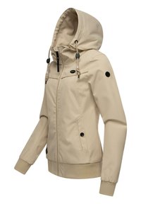 Béžová softshellová bunda s kapucňou, so zipsom na prednej strane, dvoma bočnými vreckami s čiernymi gombíkmi a elastickými manžetami. Obsahuje nastaviteľné šnúrky.