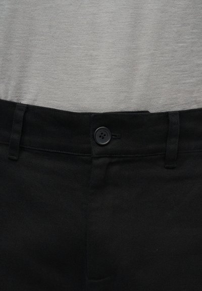 Μαύρη ζώνη παντελονιού με κουμπί και θηλιές ζώνης πάνω από απαλό γκρι ύφασμα.