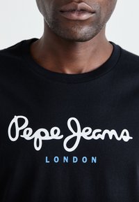 Sort bomulds T-shirt med et hvidt skriftlogo, der står "Pepe Jeans" over "LONDON" i mindre blå tekst. Klassisk rund hals.