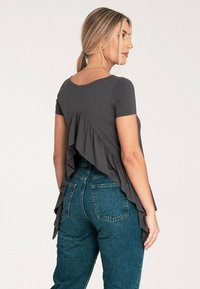 Szara bluzka z krótkim rękawem, z falbaną na tylnym hemie, połączona z niebieskimi dżinsami z wysokim stanem. Gładka tekstura; casualowy design.