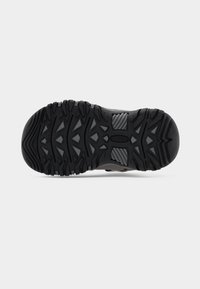 Σόλα παπουτσιού πεζοπορίας με βαθιά ανάγλυφα πέλματα, μαύρο καουτσούκ και γκρι λεπτομέρειες· σχεδιασμένη για πρόσφυση και ανθεκτικότητα σε ανώμαλες επιφάνειες.